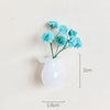 A small white glass vase holding light blue flowers, displayed against a neutral background.