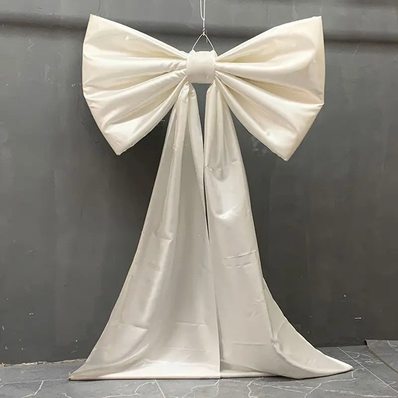 A large white satin bow with long tulle drape used for event decoration.