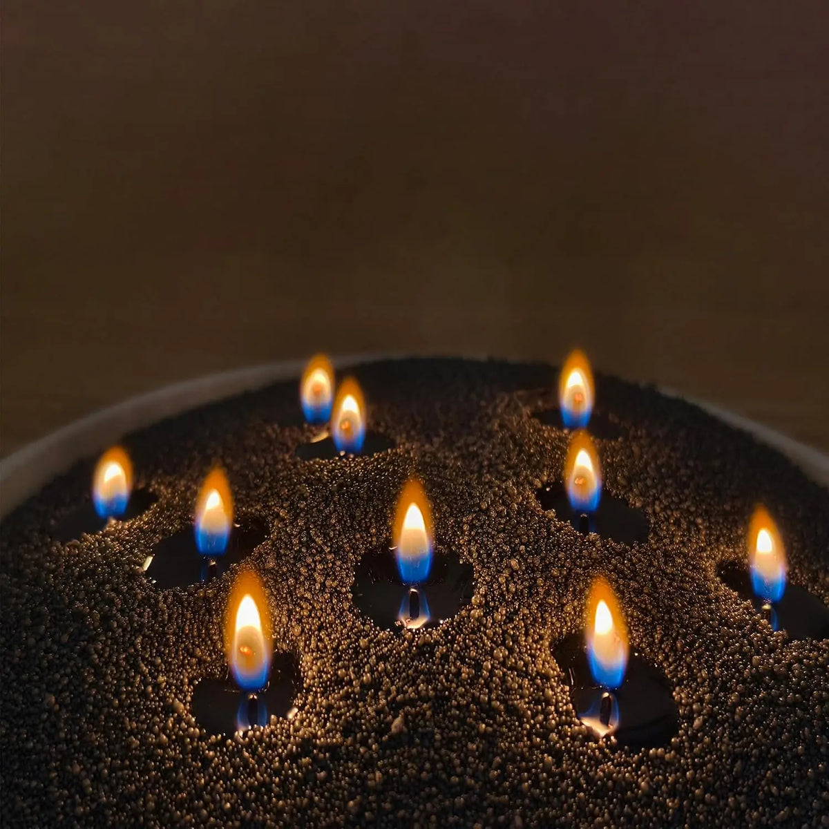 A close-up of a black pearled candle with multiple lit wicks casting warm light on the surface.