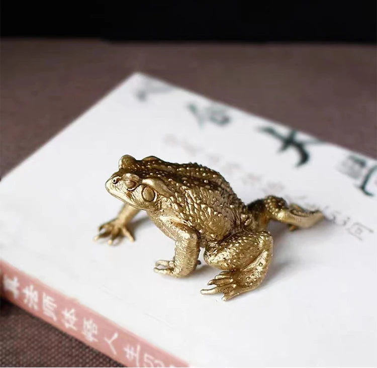 A brass money frog feng shui figurine resting on a white book page.
