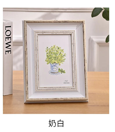 A framed watercolor painting of green foliage in a blue vase displayed on a wooden table.