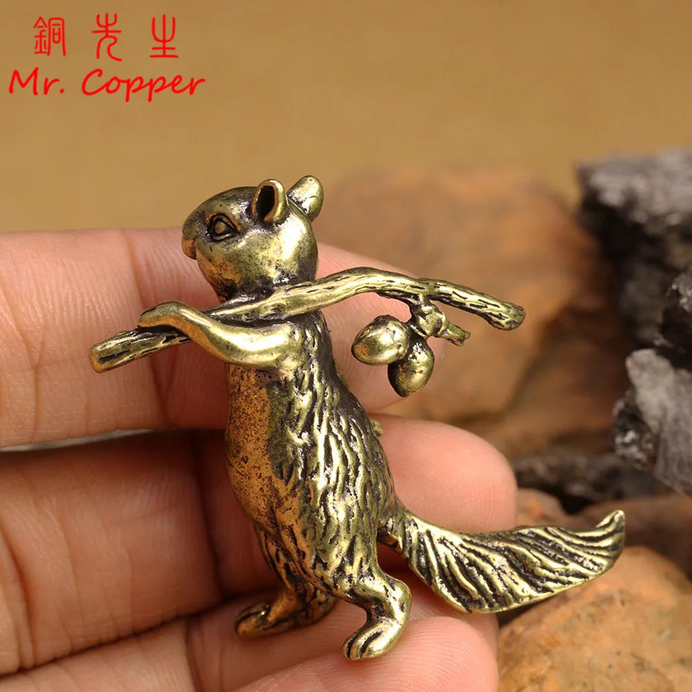 A vintage brass squirrel figurine is held in a hand against a blurred background of rocks.