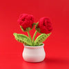Hand woven crochet red roses potted in a white ceramic cup against a red background