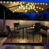 A patio umbrella light illuminates a dark outdoor dining area with string lights above a wooden table and chairs.