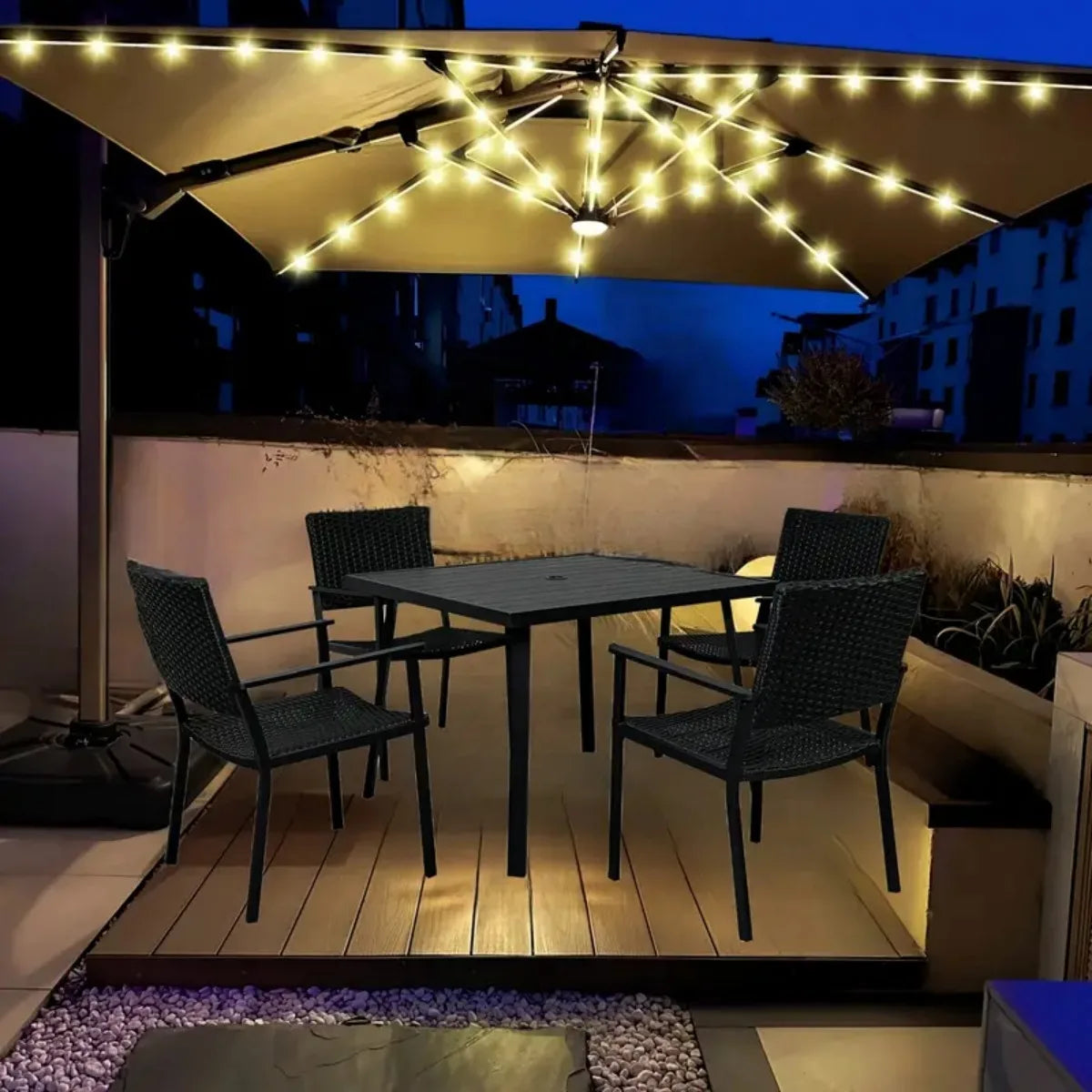 A patio umbrella light illuminates a dark outdoor dining area with string lights above a wooden table and chairs.
