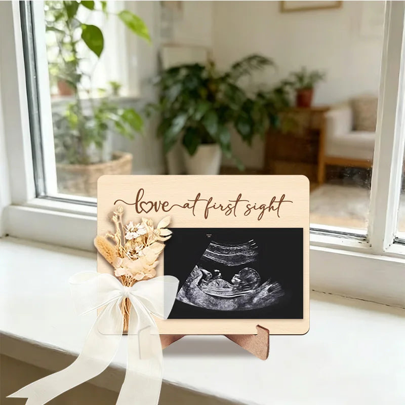 A wooden ultrasound photo frame with a ribbon, featuring text that reads love at first sight.