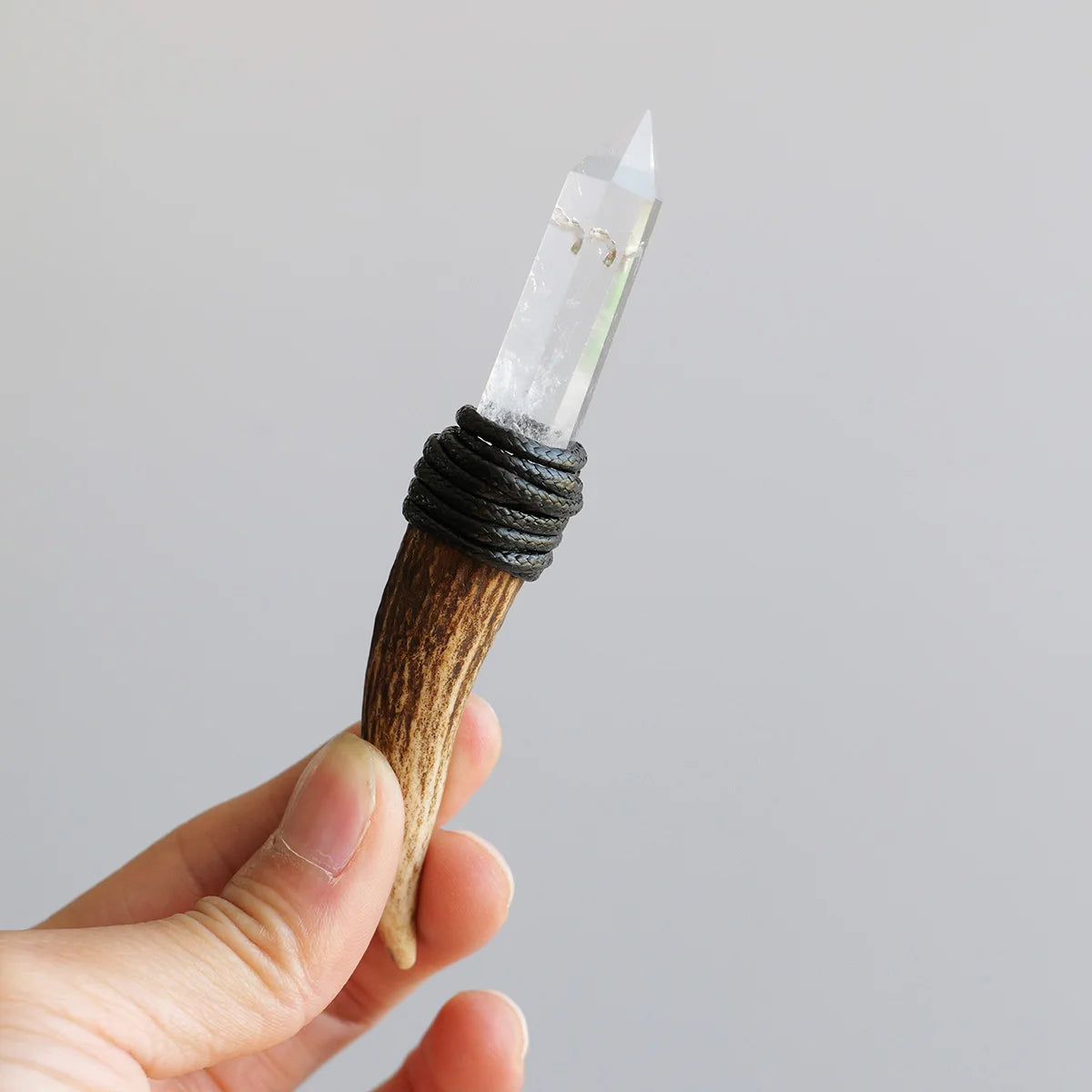 A hand holds a natural crystal Herkimer scepter wand with a wooden handle and clear crystal tip.