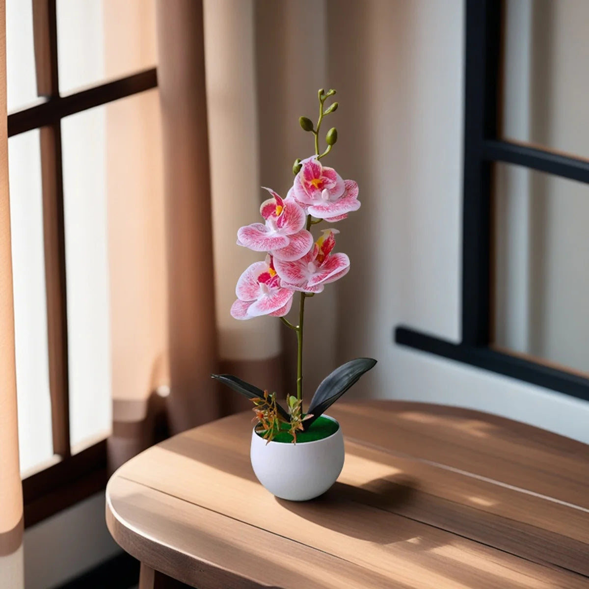 A realistic artificial orchid plant with pink flowers in a white pot sits on a wooden table near a window.