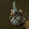 A hand holds a traditional ceramic wine gourd with a stopper and a decorative woven net.