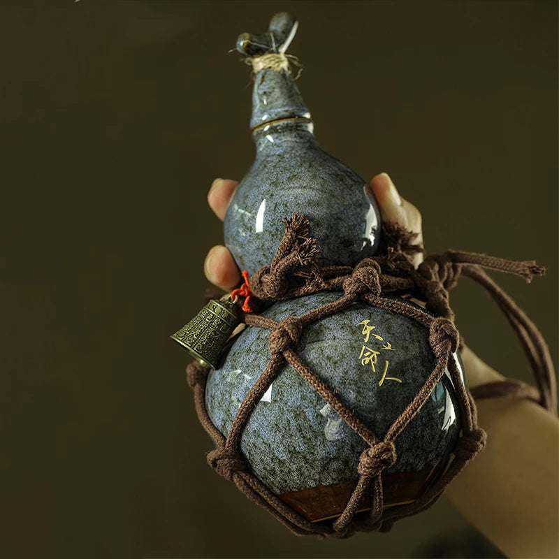 A hand holds a traditional ceramic wine gourd with a stopper and a decorative woven net.