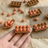 A hand holds a small wooden tray filled with miniature egg-shaped items and several molded plastic egg trays.