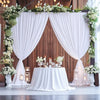 A white draped curtain backdrop decorated with greenery and white flowers for a wedding or event setting.
