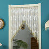 A sheer lace door curtain with gold tassels hangs in a white frame against a teal wall.