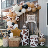 A balloon arch display featuring brown, white, and gold balloons with cow print patterns and natural wood elements.