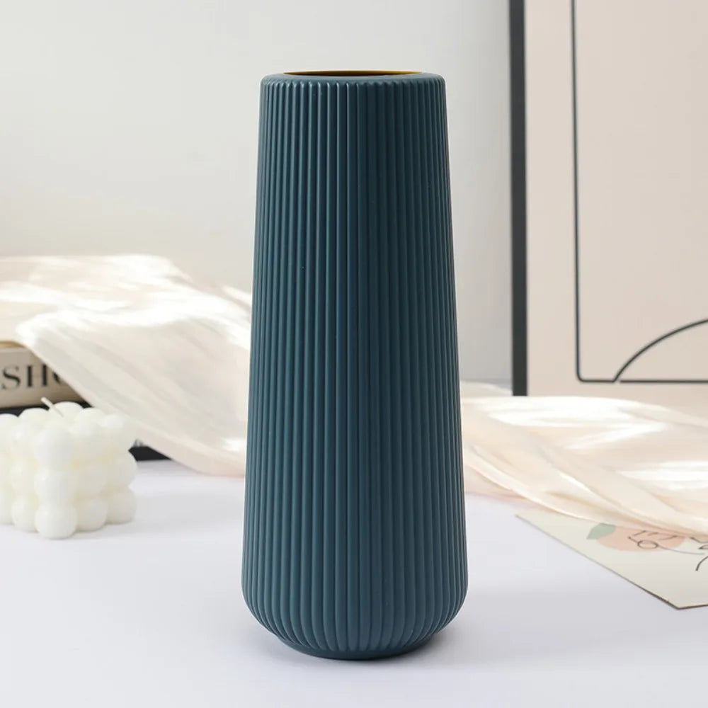 A tall, ribbed, dark teal plastic vase with a matte finish sitting on a white surface next to light beige fabric.
