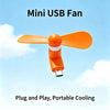 An orange mini USB fan with soft blades is shown against a light blue sky background.