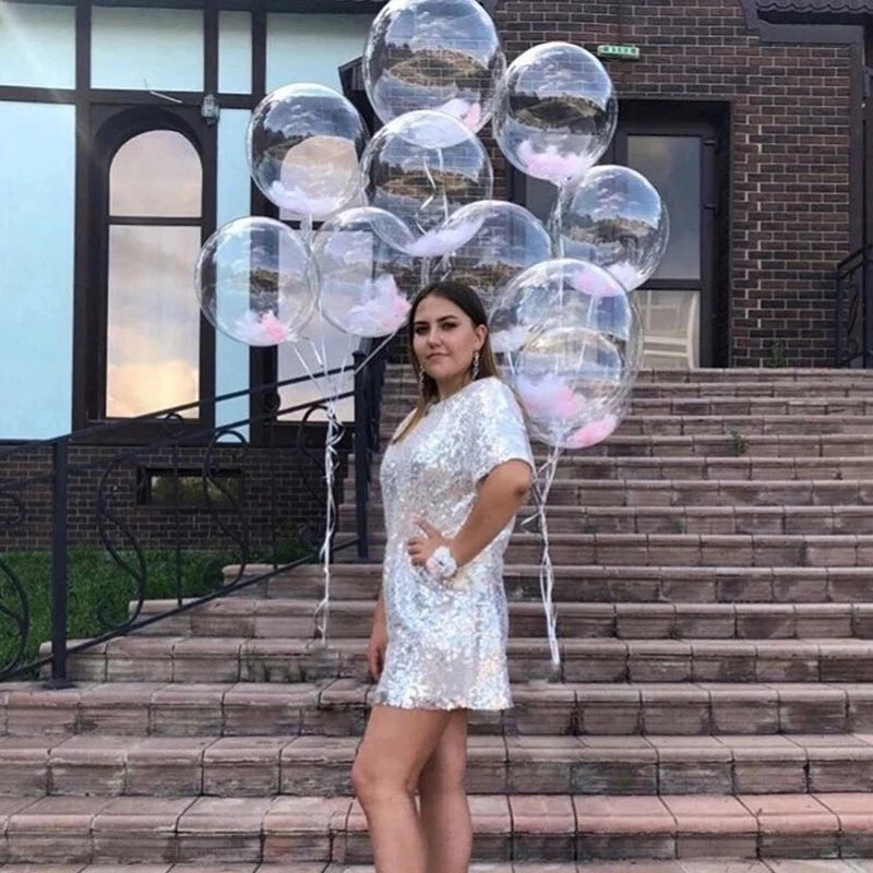 A woman in a silver sequined dress stands on stone steps surrounded by clear and pink bubble balloons.