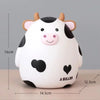 A white cartoon cow figurine with black spots and pink features, used as a piggy bank or coin holder.