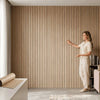A woman stands in a room with vertical wood-grain wallpaper, gesturing toward the wall.