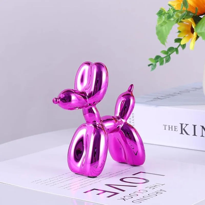 A shiny pink resin balloon dog sculpture used as whimsical decor on a white surface.