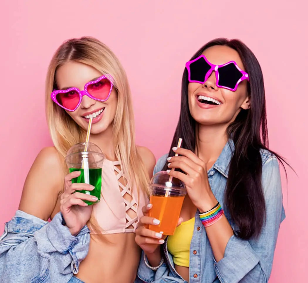 Two women smiling while holding glow-in-the-dark silicone bracelets and colorful drinks.