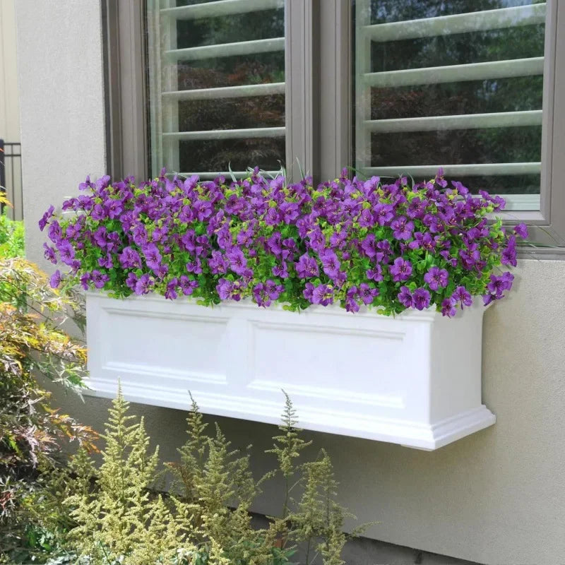 A window box filled with vibrant purple petunia flowers mounted on a light-colored exterior wall.