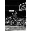 A black and white photo of a basketball player during a game, focusing on the action under a hoop.