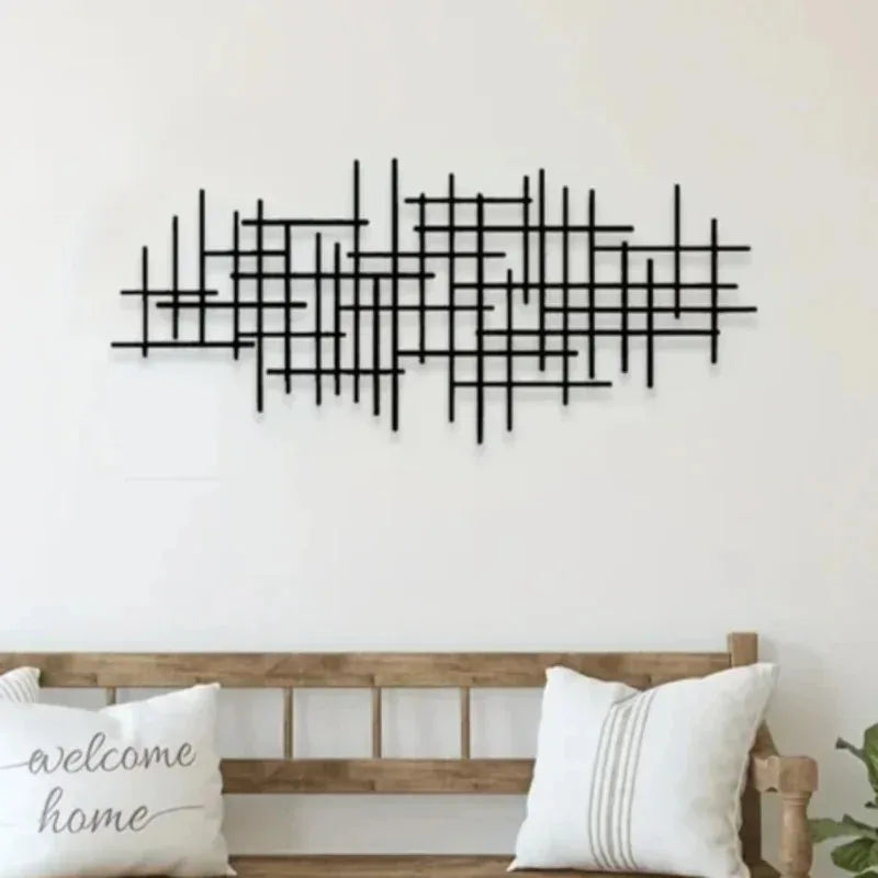 Black geometric metal wall art sculpture with intersecting lines mounted on a white wall above a wooden bench.