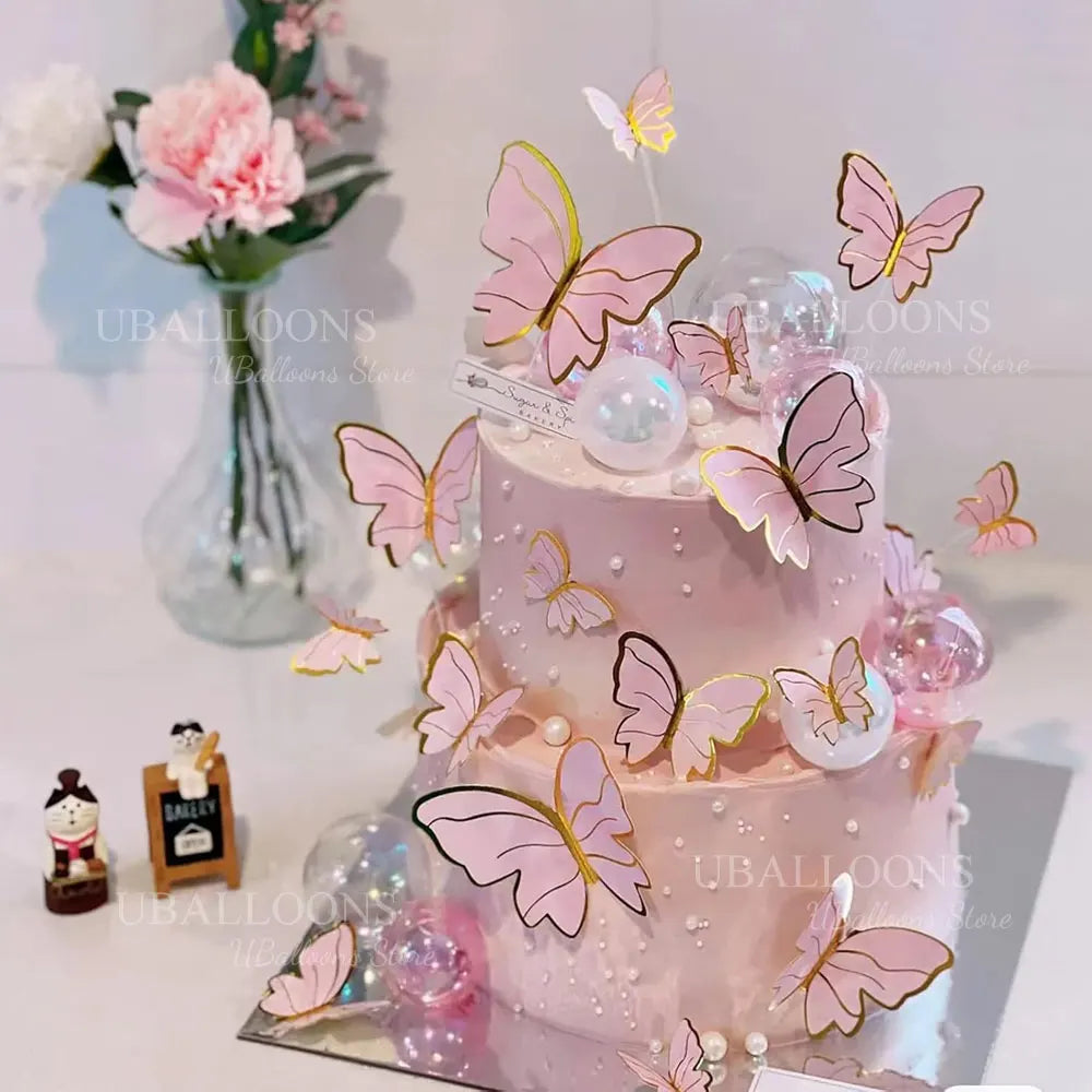 A tiered pink cake decorated with gold and pink butterfly toppers on a white background.