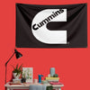 A black flag with the white Cummins logo printed on it, displayed on a red wall.
