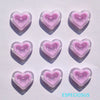A set of six translucent pink heart-shaped acrylic charms casting shadows on a white surface.