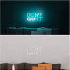 A glowing neon sign on a dark wall reads DON'T QUIT, displayed above a sofa.