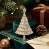 A sparkling rhinestone Christmas tree brooch pin displayed on a green velvet surface with pine cones and a gift box.