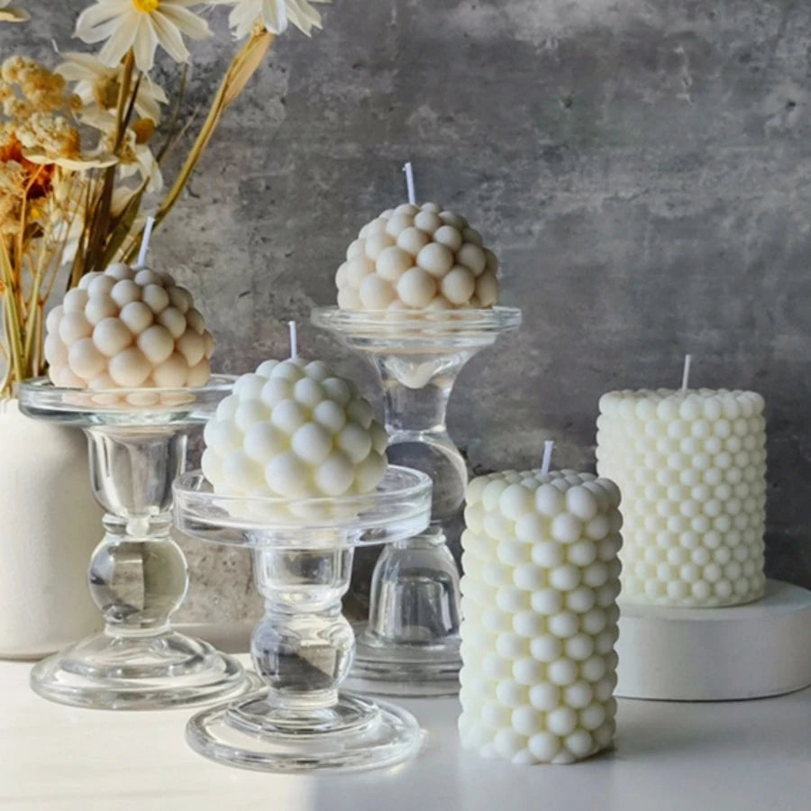 A white Nordic bubble scented soy candle is displayed next to dried flowers on a gray textured background.