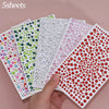 A hand holds a collection of colorful glitter gem stick-on facial tattoos in various shades and sizes.