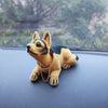 A small, tan and black dog ornament figure wearing a gold chain is placed on a dark surface.