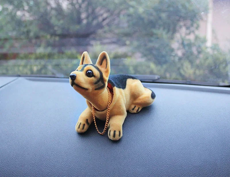 A small, tan and black dog ornament figure wearing a gold chain is placed on a dark surface.
