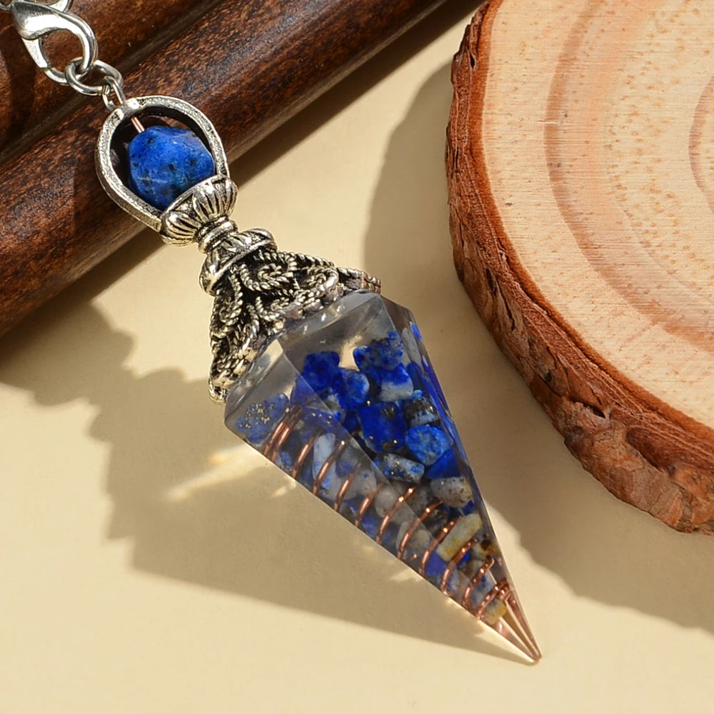 A crystal pendulum with a blue bead and silver chain rests on a wooden board.