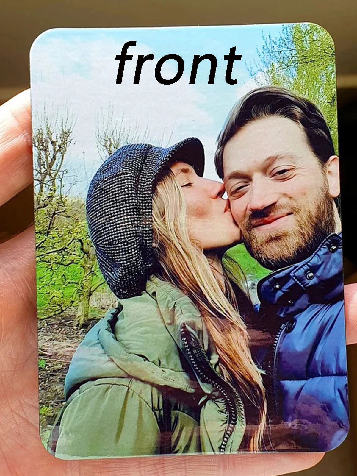 A photo of a couple kissing, featuring a woman with long hair and a man with a beard, set against a natural outdoor backgroun
