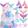 A tiered cake decorated with purple and pink mermaid tail toppers, seashells, and starfish.