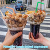 A hand holds a purple drink in a plastic cup with a straw, next to a bowl of food and a green straw.