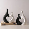 Three modern heart-shaped ceramic vases in black and white on a light surface.