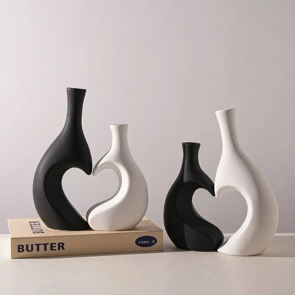 Three modern heart-shaped ceramic vases in black and white on a light surface.