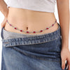 A woman wearing a denim skirt and light top displays a delicate red crystal waist chain.