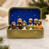 A hand-painted mini nativity set featuring figures in a gold tin storage box against a blue starry background.