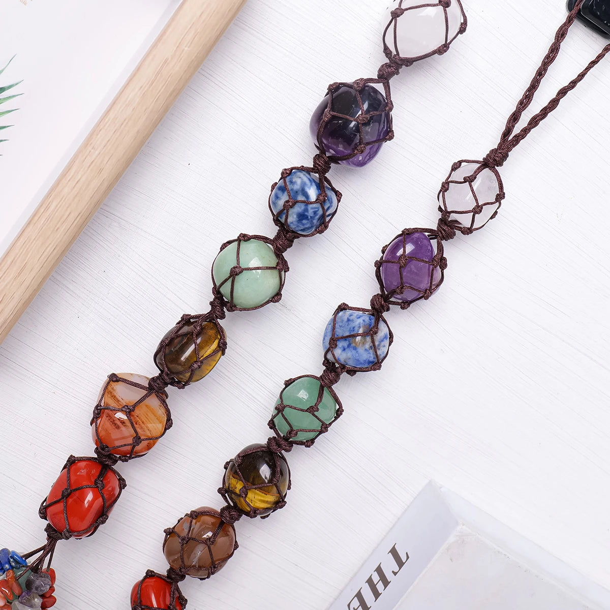 A string of natural crystal rolling stone pendants in various colors like purple, blue, and green on a white background.