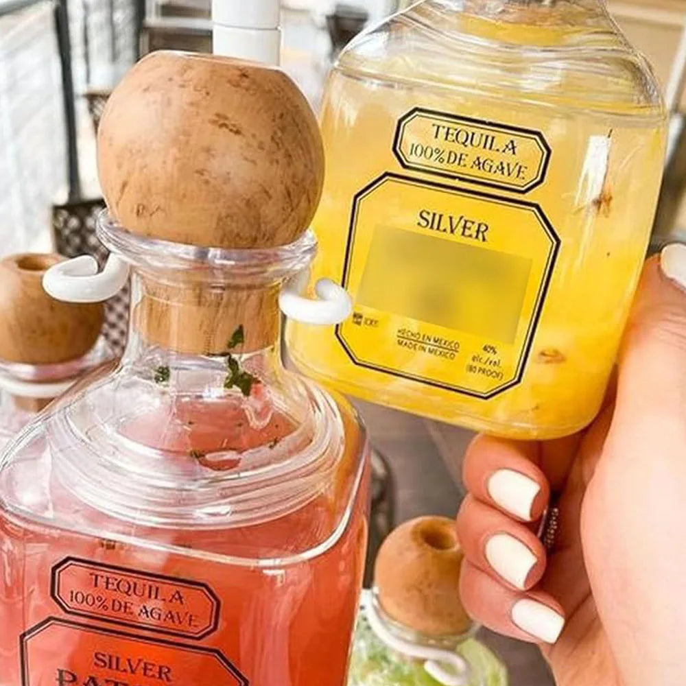 A hand holds two reusable plastic drinking bottles of silver tequila and agave, showing the liquid inside.