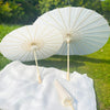 Two white decorative paper parasols open on a green lawn, resting on a white cloth.