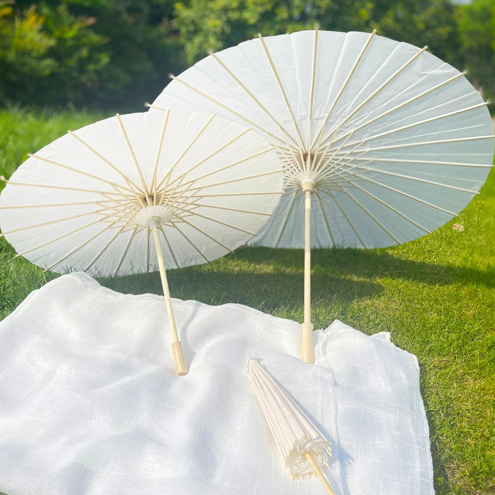 Two white decorative paper parasols open on a green lawn, resting on a white cloth.