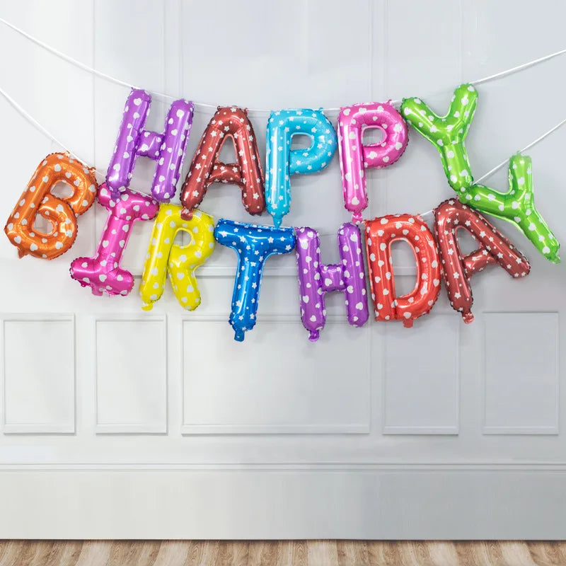 A garland of colorful foil letter balloons spelling out Happy Birthday strung across a white wall.